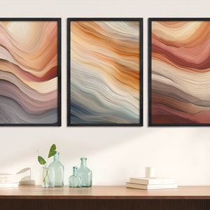 May include: Three abstract art prints with a layered, wavy pattern in shades of brown, beige, and gray. The prints are framed in black and hung on a white wall.