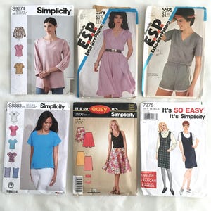 May include: Five different sewing patterns for clothing. The patterns are from Simplicity and include a pink top, a purple dress, a gray jumpsuit, a blue top, and two dresses with floral prints.