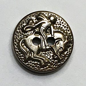 May include: A silver-toned button with a detailed relief of a rider on horseback. The button has two holes for sewing and a textured border. The design is intricate and the button appears to be made of metal.
