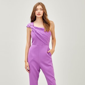 May include: A purple one-shoulder jumpsuit with a knotted detail on the shoulder strap. The jumpsuit has a straight leg and is made of a smooth fabric.