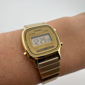 K&ouml;nnte beinhalten: Eine goldfarbene digitale Casio-Uhr mit rechteckigem Zifferblatt und passendem Metallarmband. Die Uhr zeigt die Zeit 12:29:38 an. Auf dem Zifferblatt stehen die W&ouml;rter "CASIO", "ALARM", "TIMER", "MODE", "START STOP" und "WATER WR RESIST".