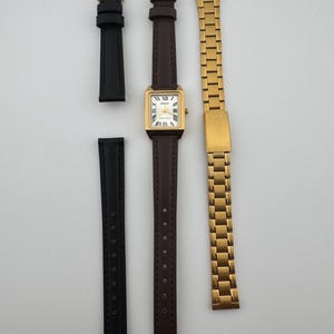 May include: A gold-toned Casio watch with a rectangular face and Roman numeral hour markers, paired with a brown leather strap, a black leather strap, and a gold metal band. The watch face displays the Casio brand name.