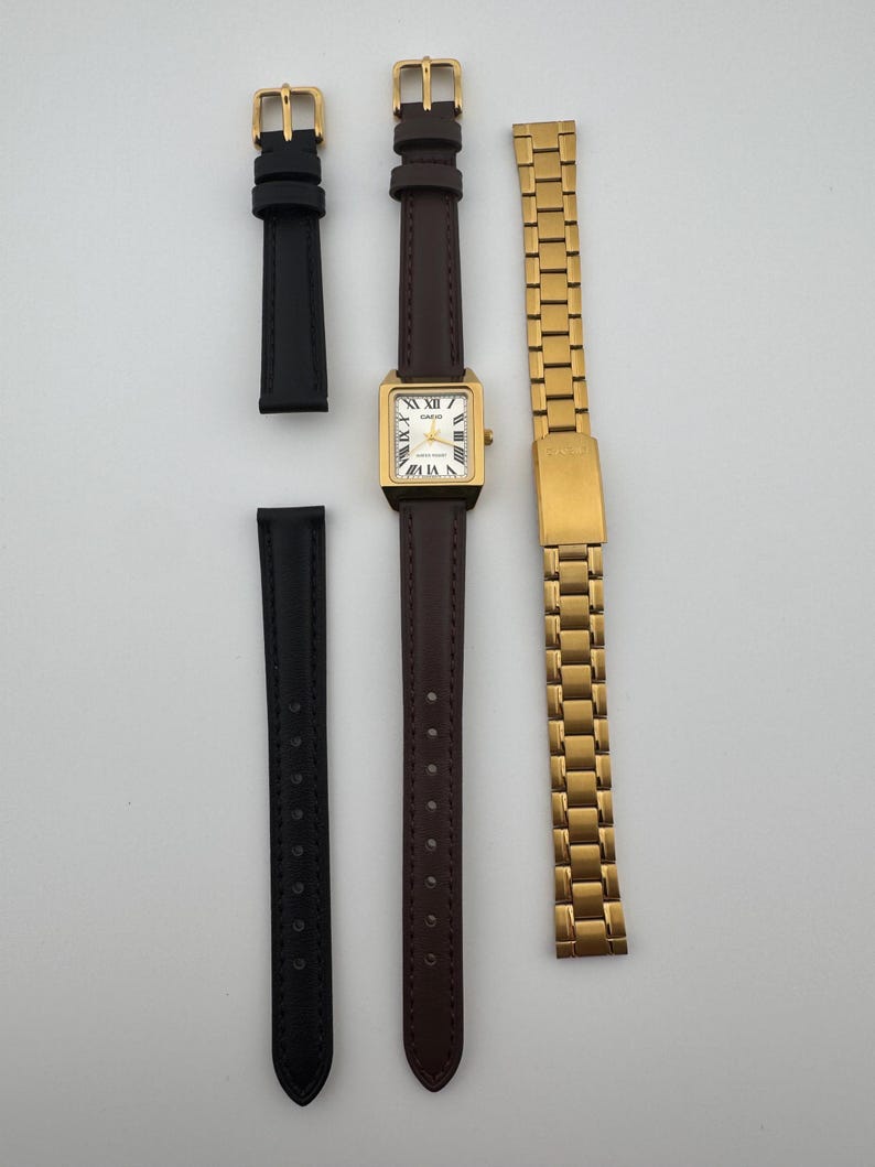 May include: A gold-toned Casio watch with a rectangular face and Roman numeral hour markers, paired with a brown leather strap, a black leather strap, and a gold metal band. The watch face displays the Casio brand name.