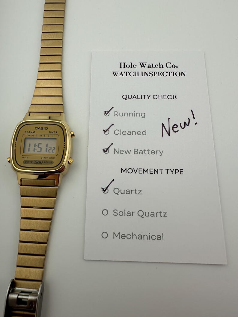 May include: A gold-toned Casio digital watch with a rectangular face and a matching metal band. The watch displays the time 11:51:22. A white card next to the watch reads "Hole Watch Co. WATCH INSPECTION" and lists quality checks.