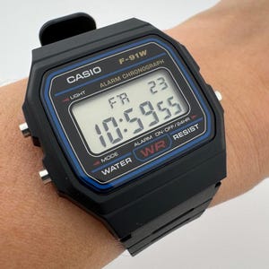 May include: Black Casio F-91W digital watch with a rectangular face and black strap. The watch face displays the time, day, and date. Features include alarm and chronograph functions. The watch is water-resistant.