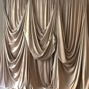 May include: A set of elegant, champagne-colored curtains. The fabric drapes in soft folds, creating a luxurious and flowing aesthetic. The curtains are hung from a rod and cascade down, adding a touch of sophistication to any room.