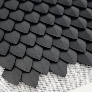 May include: A close-up of a black, textured, scale-like material. The material is arranged in a repeating pattern of overlapping scales, creating a visually interesting and tactile surface.