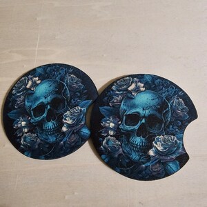 May include: Two round black coasters with a blue skull and floral design. The skull is surrounded by blue roses and leaves.