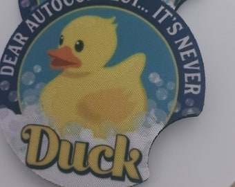 May include: Two round blue and white coasters with a yellow rubber ducky in the center. The coasters have the text "Dear Autocorrect... It's Never Duck" on them.