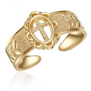 Puede incluir: Anillo ajustable dorado con un diseño de cruz en un marco ovalado decorativo. La banda del anillo está texturizada con un patrón de hojas.