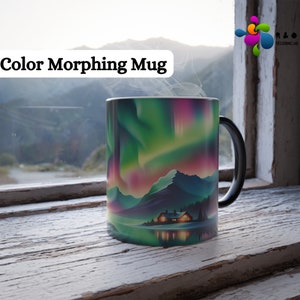May include: A black mug with a color-changing design featuring a landscape with a cabin and a lake under a colorful aurora borealis. The mug is sitting on a wooden surface.
