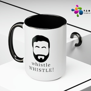 May include: White ceramic mug with a black handle and black interior. The mug features a black and white illustration of a man with a beard and the text "whistle WHISTLE!"