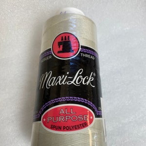 May include: A spool of Maxi-Lock All Purpose Spun Polyester thread in a light beige color. The spool is labeled with the brand name and the type of thread.