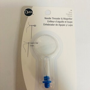 May include: A clear plastic needle threader with a magnifying glass and a blue plastic handle. The packaging says "Needle Threader & Magnifier", "Enfileur d'aiguille et loupe", and "Enhebrador de Agujas y Lupa".