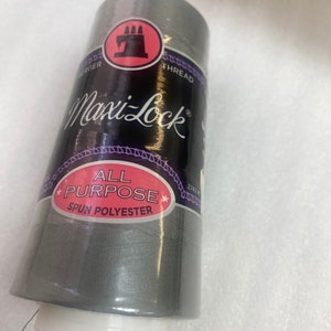 May include: A spool of gray Maxi-Lock All Purpose Spun Polyester thread. The spool has a black label with white text and a red sewing machine logo.