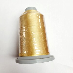 May include: A spool of gold thread wrapped in clear plastic, with a gray plastic base.