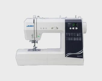 May include: A white Juki sewing machine with a black control panel. The machine has a digital display and various stitch selection options. The model number is visible on the side. It is designed for sewing projects.