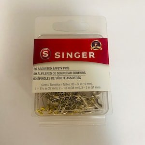 May include: A clear plastic package containing 50 assorted safety pins in various sizes. The package is labeled "Singer" and includes the sizes of the pins in inches and millimeters. The package is on a white background.