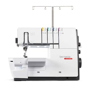 May include: White overlock sewing machine with a black base and a silver needle bar. The machine has a clear plastic cover over the needle area and a black control panel with the text "bernette swiss design" on it. The machine is labeled "b62 deluxe".