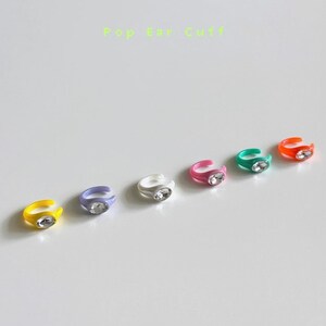 May include: Six colorful plastic ear cuffs with clear rhinestones. The ear cuffs are in the colors yellow, purple, white, pink, green, and orange.