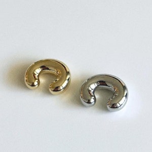 May include: Two bean ear cuffs, one gold and one silver, on a white background. The text "BEAN EAR CUFF" is above the cuffs, and the text "FLAT" is below the cuffs.