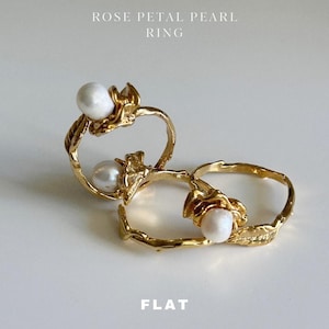 May include: Two gold rings with a pearl on each. The rings are designed to look like a rose petal. The text "ROSE PETAL PEARL RING" is above the rings and the text "FLAT" is below the rings.