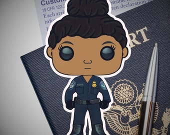 May include: A sticker of a cartoon figure in a dark blue uniform with a badge, standing in front of a passport and a pen. The sticker has a Homeland Security logo and the word "Custom" is visible.