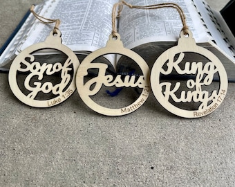 May include: Three wooden Christmas ornaments with religious text. The ornaments are round and have a string attached to the top. The text on the ornaments reads "Son of God Luke 1:35", "Jesus Matthew 1:21", and "King of Kings Revelation 17:14".