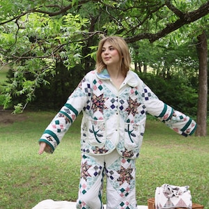 Op de afbeelding: Een bijpassende tweedelige set bestaande uit een jasje met lange mouwen en knopen en een wijde broek, gemaakt van een patchwork quilt met sterpatronen, bloemenprints en effen witte panelen met groene biezen en twee voorzakken.