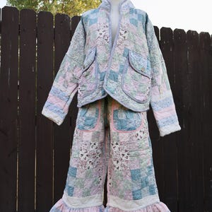 Puede incluir: Un conjunto acolchado de dos piezas que incluye una chaqueta de manga larga y pantalones anchos. El conjunto está confeccionado con un patchwork de telas florales y geométricas en tonos azul claro, rosa y blanco, con dobladillos con volantes.