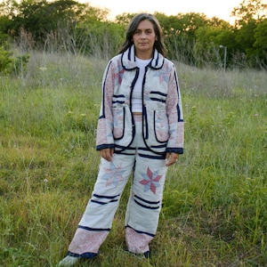 May include: A quilted jacket and matching wide-leg trousers set featuring a light cream base with pink and blue star-shaped patchwork patterns, accented by dark navy blue trim and a white undershirt, creating a coordinated two-piece outfit.