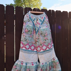 Puede incluir: Pantalones acolchados de pierna ancha con diseño de patchwork, estampados florales en rosa, verde y blanco, acentuados con un estampado de celosía rosa, dos bolsillos de parche, cintura elástica y bajos con volantes y borde festoneado.