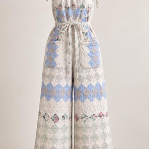 May include: A quilted jumpsuit featuring a patchwork diamond pattern in shades of light blue, sage green, and floral prints. The garment has a scoop neckline, tie-up shoulder straps, a drawstring waist, two front patch pockets, and a scalloped hem.