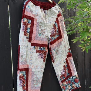 Könnte beinhalten: Gesteppte Hose mit einem Patchwork-Log-Cabin-Design aus verschiedenen Blumen- und geometrischen Mustern in Dunkelrot, Creme, Rosa und Marineblau. Die Hose hat einen weiten Schnitt und einen elastischen Bund mit einem dunkelroten Saum.