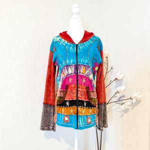 May include: A colorful zip-up hoodie with a vibrant design. The jacket features a turquoise body with a red hood and sleeves. The front has a patchwork design with pink, orange, and black sections, embellished with embroidered details and floral accents.