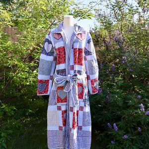 May include: A long-sleeved quilted robe featuring a patchwork design of red, white, and blue fabrics. The pattern includes gingham checks, paisley prints, and heart-shaped motifs. It has a collared neckline and a matching fabric tie belt at the waist.