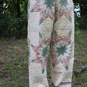 May include: Quilted pants featuring a patchwork design with star and floral patterns in cream, pink, and green. The pants have a wide-leg cut and are made from a soft, quilted fabric, offering a unique, vintage aesthetic.