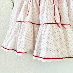 May include: White polka dot skirt with red trim and ribbon accents. The skirt features a tiered design with red ribbon and lace trim along the hemline. The fabric is a lightweight material with small red polka dots.