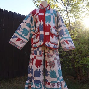 May include: A two-piece quilted outfit consisting of a long-sleeved jacket and wide-leg pants. The set features a patchwork pattern in red, teal, blue, and white, with floral fabric accents, a mandarin collar, and ruffled pant hems.