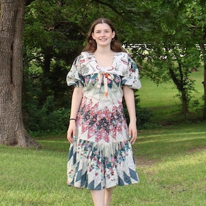 Peut inclure: Robe de style vintage avec un motif patchwork. La robe présente un col en V, des manches courtes bouffantes et une jupe midi. Le tissu arbore des motifs floraux et géométriques dans les tons de rouge, bleu et blanc. La robe est portée à l'extérieur.