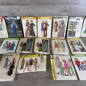 May include: A collection of vintage sewing patterns from brands like Simplicity, Butterick, and McCall's. The patterns feature illustrations of clothing designs, including dresses, jumpsuits, and coats. The covers display various colors and styles.