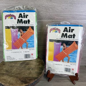 May include: Two packaged air mats. Each package is rectangular with a colorful design and the words "Air Mat". The mats are approximately 27 inches by 72 inches (69 cm x 183 cm) when deflated. One package is green, the other is pink.