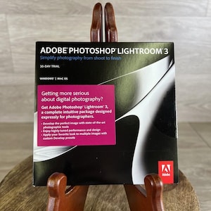 May include: A square Adobe Photoshop Lightroom 3 software box featuring a black and white abstract graphic. The text reads Adobe Photoshop Lightroom 3, Simplify photography from shoot to finish, 30-Day Trial, Windows | Mac OS, and Adobe.