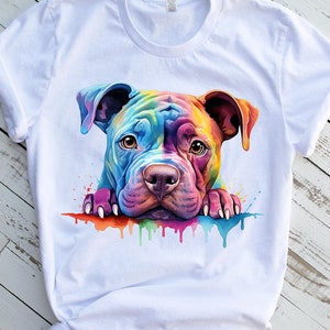 Puede incluir: Una camiseta blanca con una pintura de acuarela colorida de la cara de un perro pit bull. El perro está mirando al espectador con la lengua ligeramente fuera. La pintura tiene un esquema de color arcoíris.