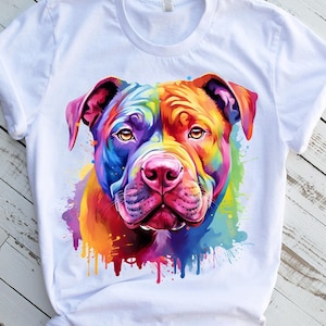 Peut inclure: Un t-shirt blanc avec une peinture aquarelle colorée du visage d'un pit-bull. La fourrure du chien est peinte dans des tons de rouge, orange, jaune, vert, bleu et violet. L'arrière-plan est une toile blanche avec des éclaboussures de couleur.