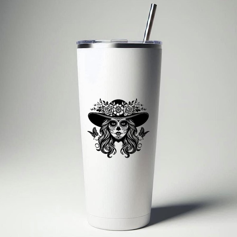 Puede incluir: Un vaso t&eacute;rmico blanco con un gr&aacute;fico en blanco y negro de una mujer con maquillaje de calavera de az&uacute;car, que lleva un sombrero adornado con flores. El dise&ntilde;o incluye mariposas y cabello rizado. Una pajita plateada est&aacute; insertada en la tapa.