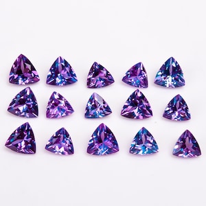 May include: A collection of 15 triangular purple and blue gemstones, arranged in rows on a white surface.