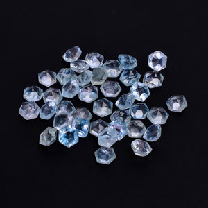 Puede incluir: Un grupo de piedras preciosas facetadas de color azul claro, probablemente aguamarina, esparcidas sobre un fondo negro. Las piedras preciosas son todas de forma hexagonal y tienen una variedad de tama&ntilde;os.