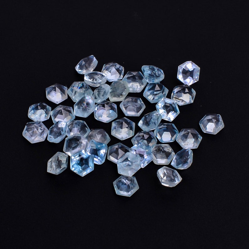 Puede incluir: Un grupo de piedras preciosas facetadas de color azul claro, probablemente aguamarina, esparcidas sobre un fondo negro. Las piedras preciosas son todas de forma hexagonal y tienen una variedad de tama&ntilde;os.