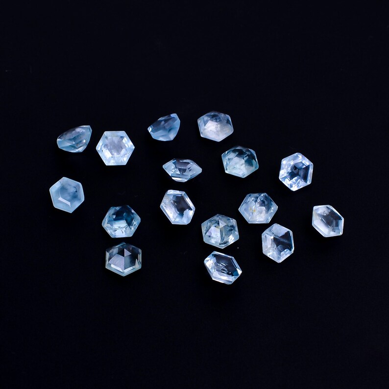 Puede incluir: Una colecci&oacute;n de 15 gemas facetadas de color azul claro, cada una con forma hexagonal, dispuestas sobre un fondo negro.